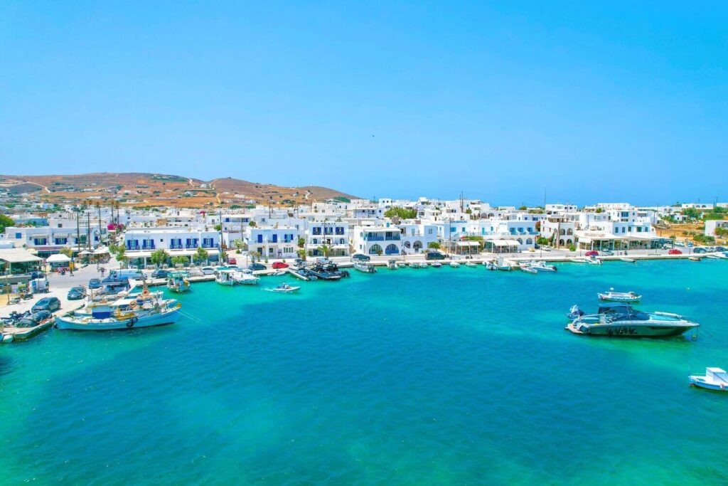 Scenic view of the coastal town and harbor in Antiparos, Greece, with boats docked along the clear blue waters.